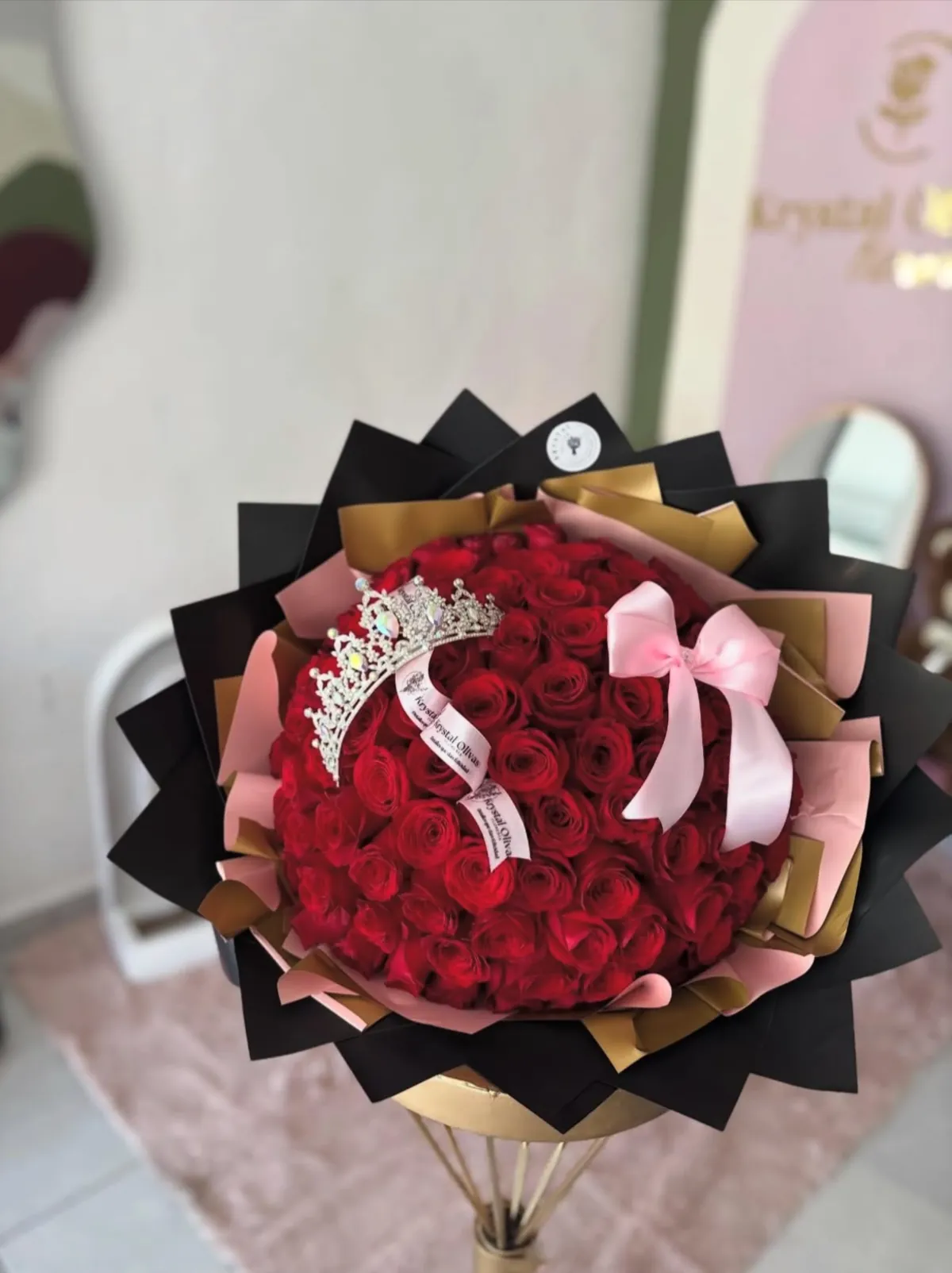Ramo de cien rosas rojas con tiara y moño rosa, envuelto en papel negro y dorado