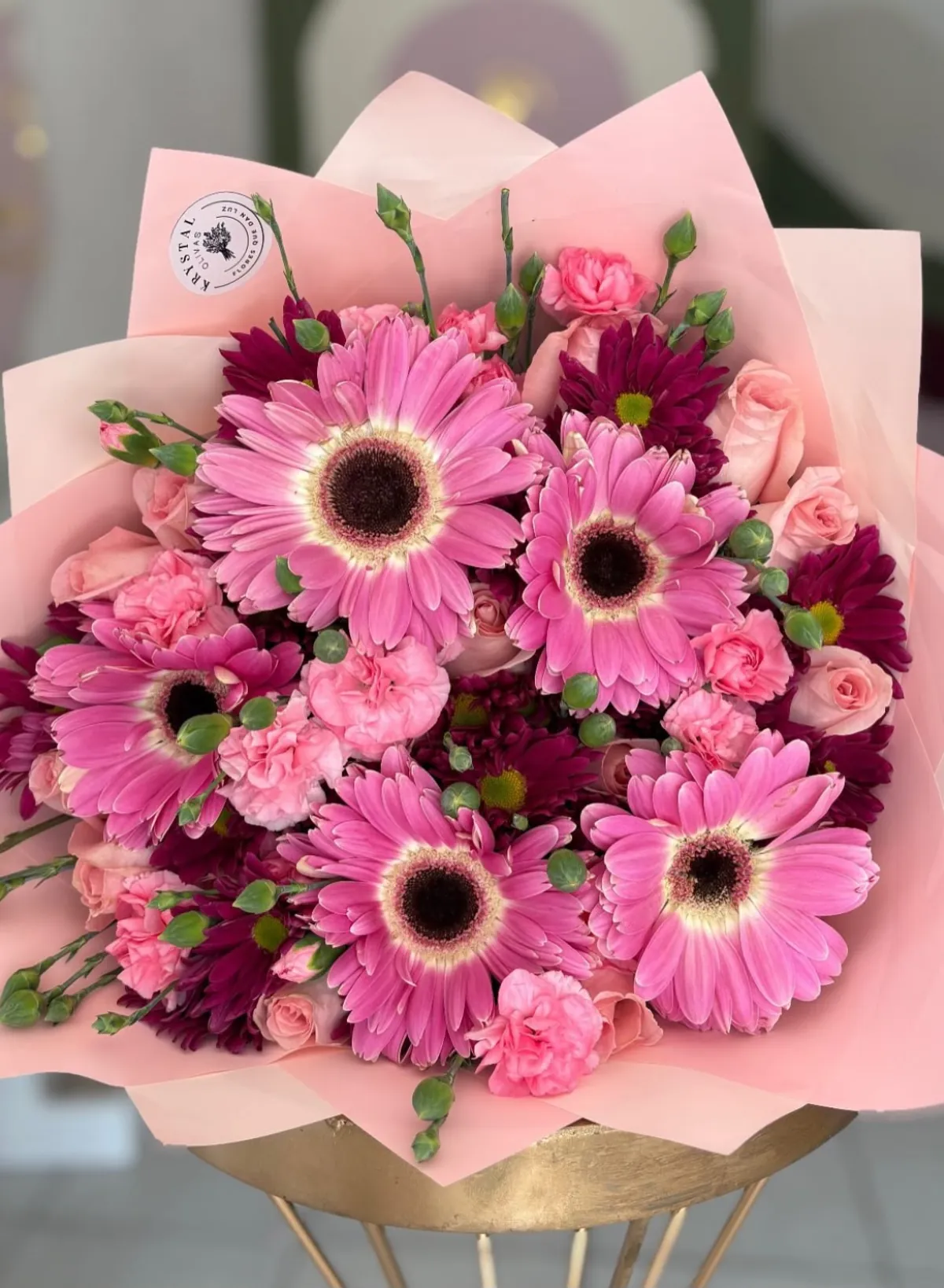 Ramo de gerberas rosa fucsia y crisantemos morados envuelto en papel rosa