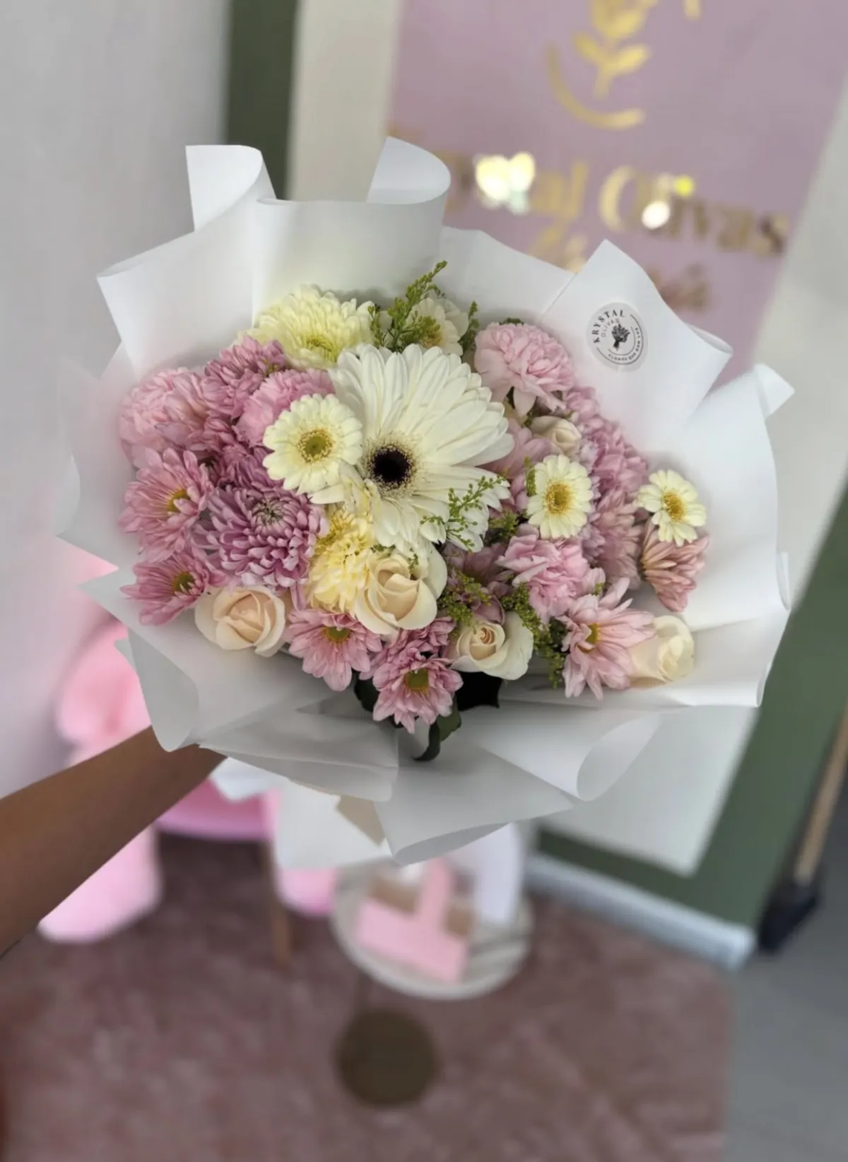 Ramo de crisantemos rosa pálido y rosas crema envuelto en papel blanco